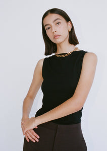 A woman wears a black, close-fitting, sleeveless knitted top. The top has a wide boat neckline.