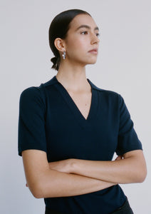A woman wears a close-fitting navy, short-sleeve knitted top. The top has a collar and a v neckline.