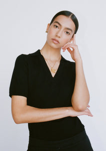 A woman wears a black, close-fitting, short-sleeve knitted top. The top has a collar and a v neckline.