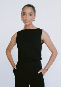 A woman wears a black, close-fitting, sleeveless knitted top. The top has a wide boat neckline.