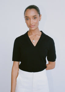 Woman wears a black, close-fitting, short-sleeve knitted top. The top has a collar and a v neckline.